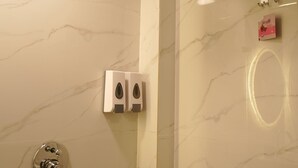 Baño con pared de mármol, dispensador de toallas, dispensador de jabón y cabezal de ducha.