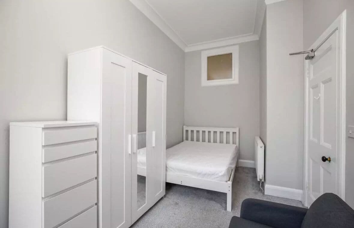 A bedroom with a white wardrobe, a bed, a radiator, and a door.