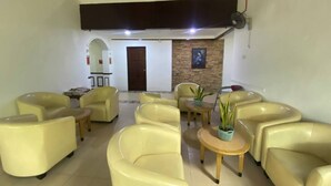 A lobby with yellow leather chairs, a small table with a plant, a door, and a wall with a framed picture.