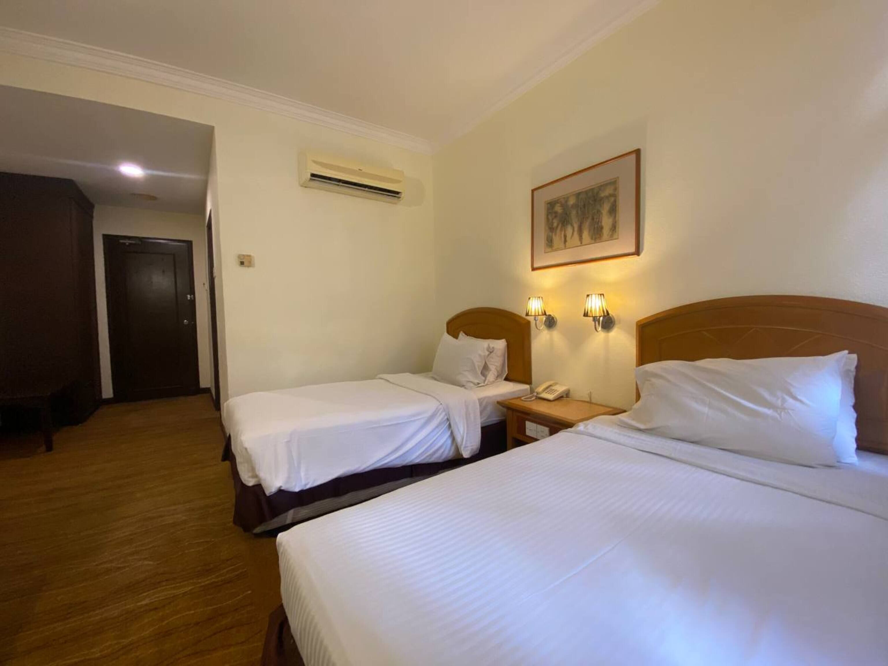 A hotel room with two beds, a bedside table with a phone, wall-mounted lamps, and an air conditioning unit.