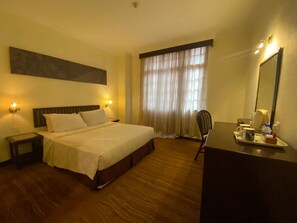 A hotel room with a bed, bedside lamps, a desk with a mirror, and a window with curtains. - Capital O 91179 Geopark Oriental Village (Langkawi)