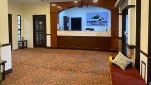 A hotel reception area with a reception desk, a large carpeted room, and a staircase leading to another floor.