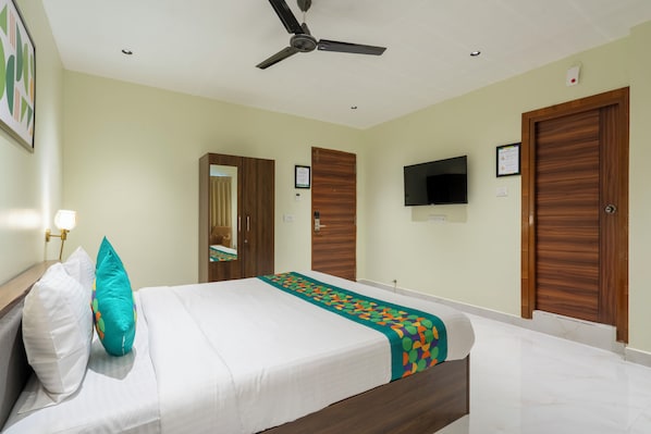A hotel room with a bed, a ceiling fan, a TV, and wooden doors. - Treebo The Infinity, Banjara Hills (Hyderabad)