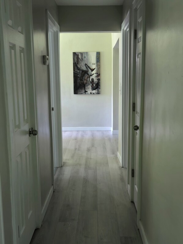 A hallway with white doors, a light-colored wooden floor, and a painting on the wall.