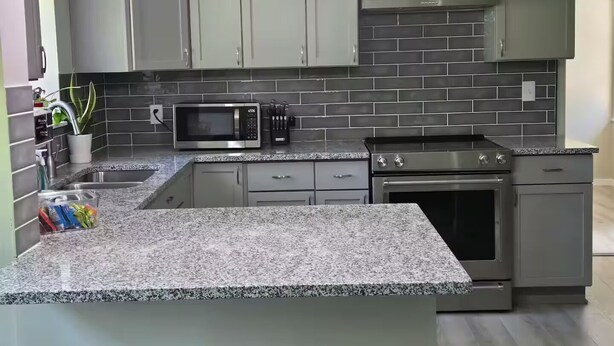 Una cuina moderna amb encimera de granit, microones integrat, electrodomèstics d'acer inoxidable i armaris grisenys.