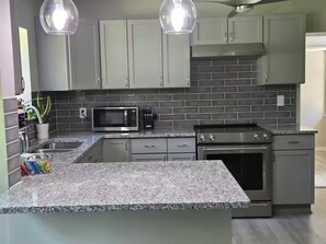 A modern kitchen with granite countertops, a built-in microwave, stainless steel appliances, and grey cabinetry.
