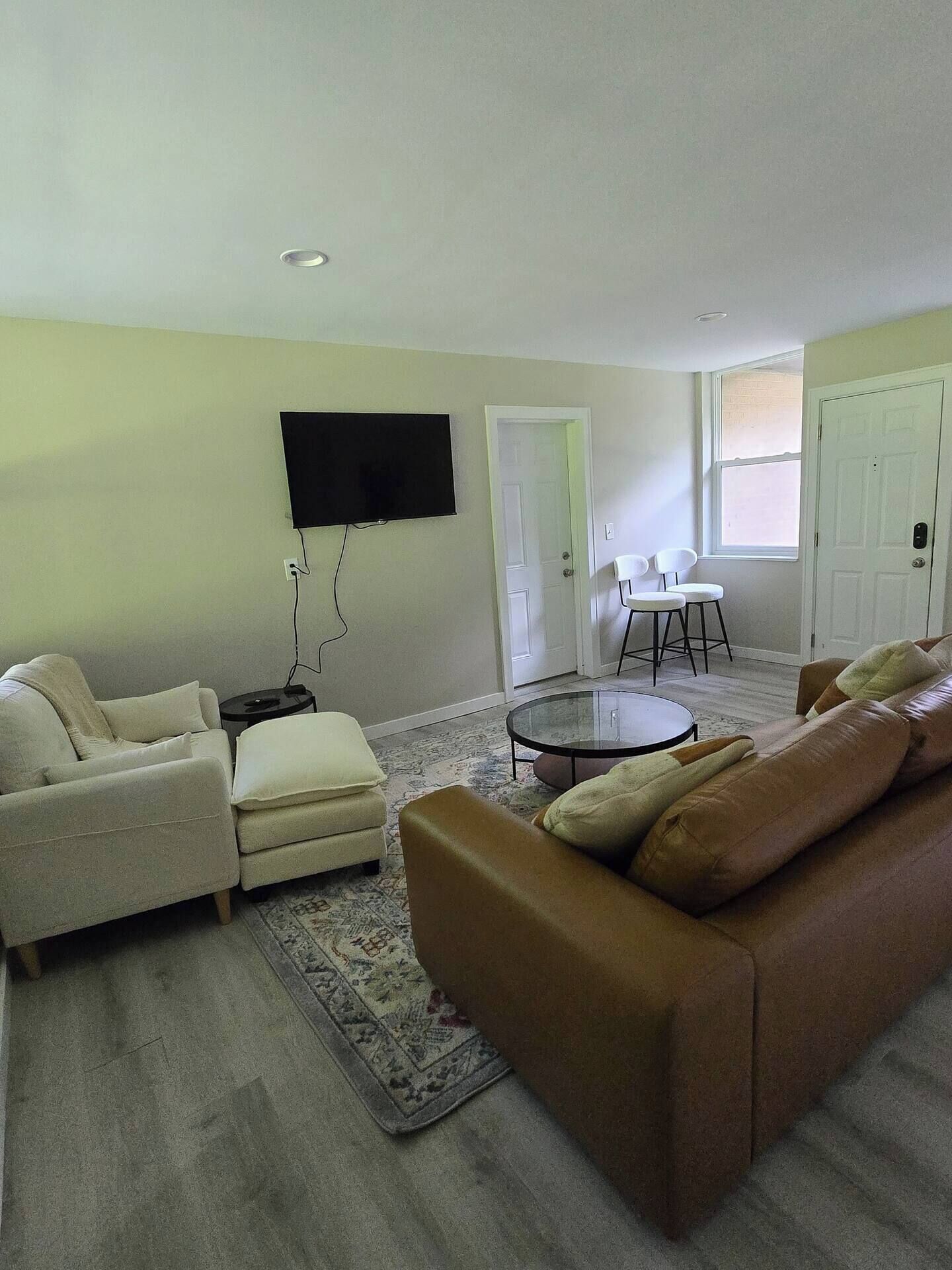 A living room with a beige sofa, a brown sofa, a small coffee table, and a flat-screen TV mounted on the wall.