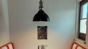 Un comedor estilo fonda con asientos tipo cabina rojos, una mesa de metal, una lámpara colgante negra y un menú en la pared.