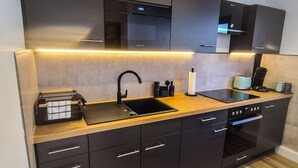 Una cocina moderna con armarios oscuros, encimera de madera, horno empotrado y pileta de acero inoxidable.