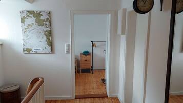 Un pasillo con suelo de madera, un mapa en la pared, un reloj y una puerta que da a otra habitación.
