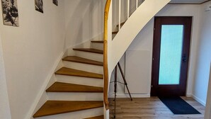 Una escalera de madera con barandillas blancas, un felpudo negro en la parte inferior y una puerta con panel de vidrio satinado.
