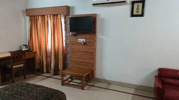 A room with a bed, a desk, a chair, a TV, and an air conditioner.