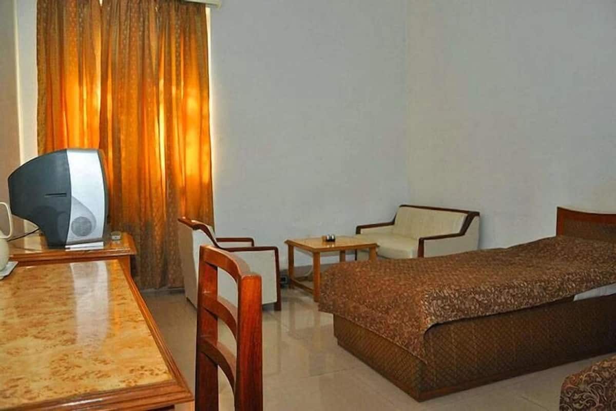 A hotel room with a bed, a desk with a computer, a chair, and a small table.