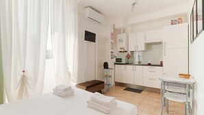 Una habitación de hotel con cama, una kitchenette pequeña, una ventana con cortinas y un baño.