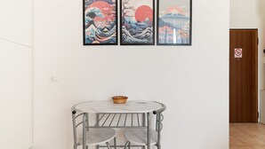 Una habitación con una mesa redonda y dos sillas, una puerta de madera y tres cuadros enmarcados en la pared.