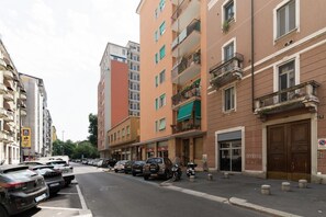 A street with parked cars, multi-story buildings, and a pedestrian. - GuestHost - Cozy Apartment near Piazza Napoli (Milan)