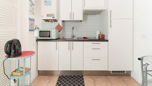 Una cocina compacta con armarios blancos, un microondas, una tetera y una pequeña mesa con un mantel rojo.