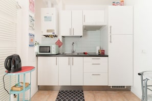 A compact kitchen with white cabinets, a microwave, a kettle, and a small table with a red mat.