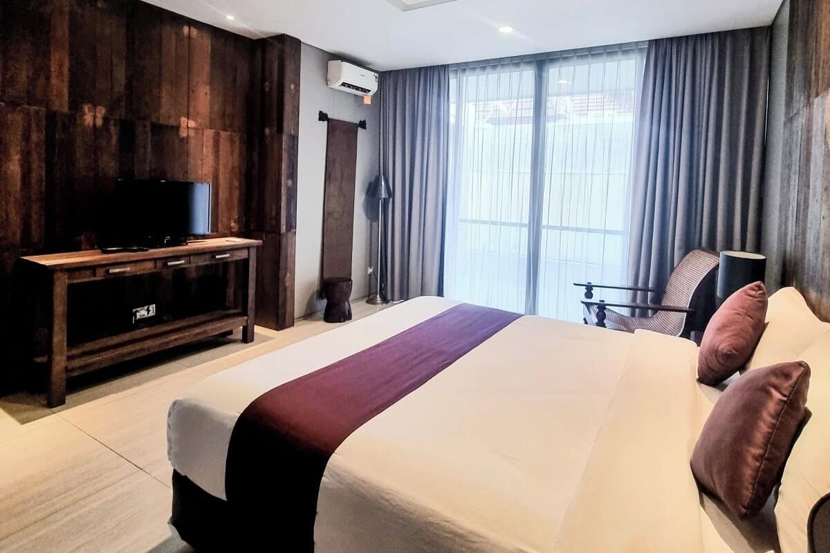 A modern hotel room with a large bed, a TV, a desk, and a window with curtains.