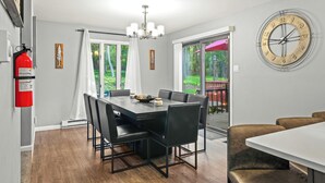 Un coin repas comprenant une grande table, des chaises, un lustre et une horloge murale.