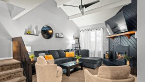 Un salon moderne avec un canapé noir, des fauteuils beiges, une table basse et une cheminée.