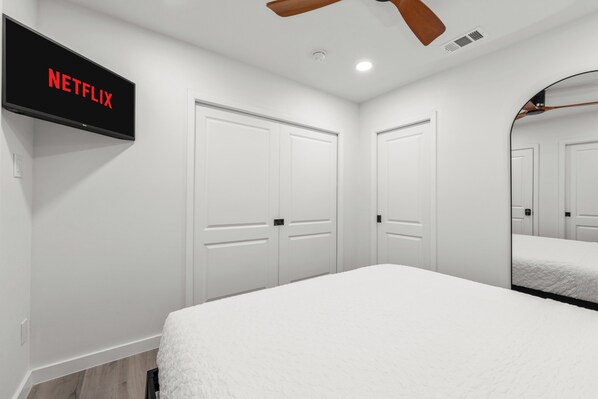 A modern bedroom with a large bed, white walls, and a mounted TV displaying 'NETFLIX'.
