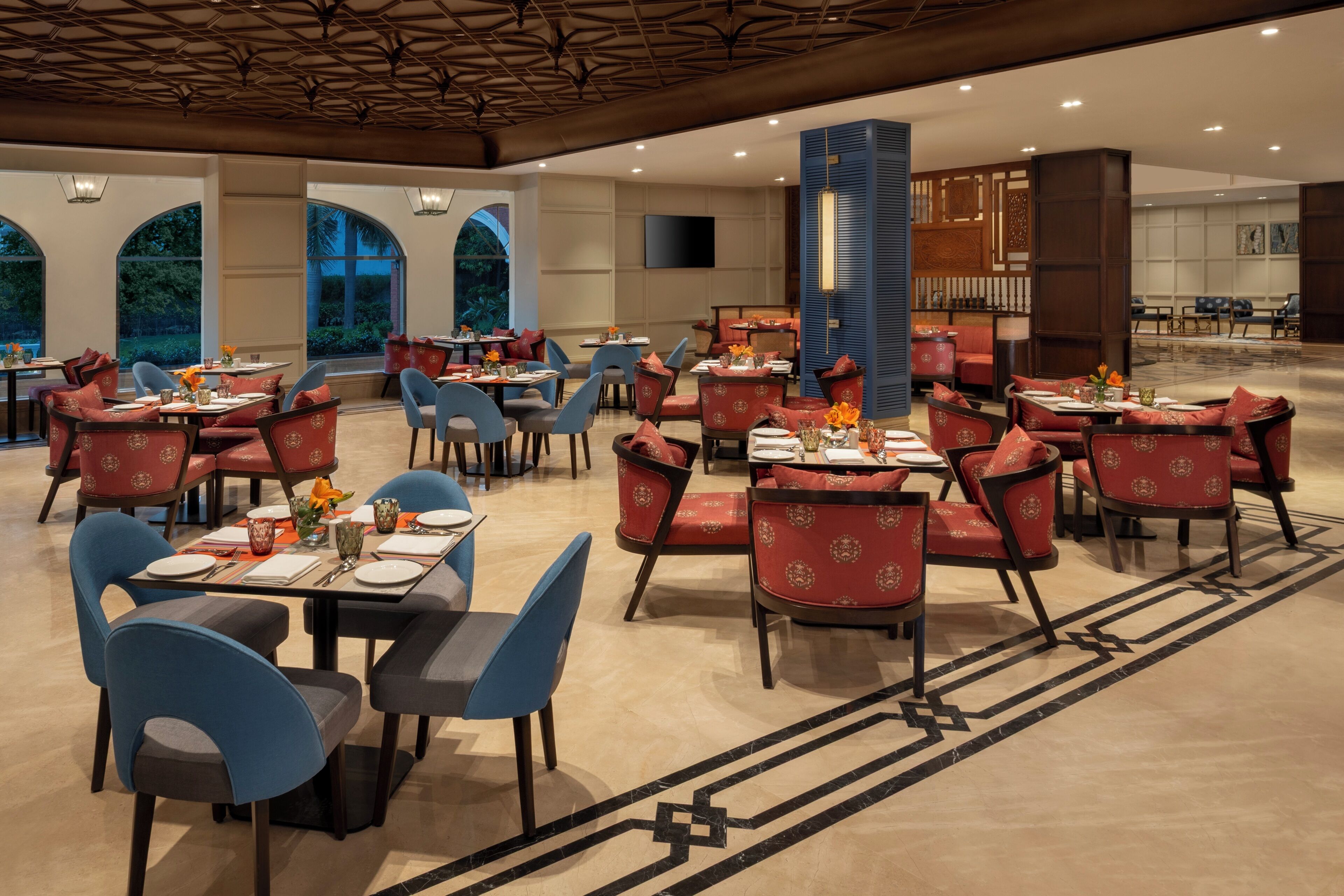 A spacious restaurant with multiple tables and chairs, large windows, and a modern ceiling design.