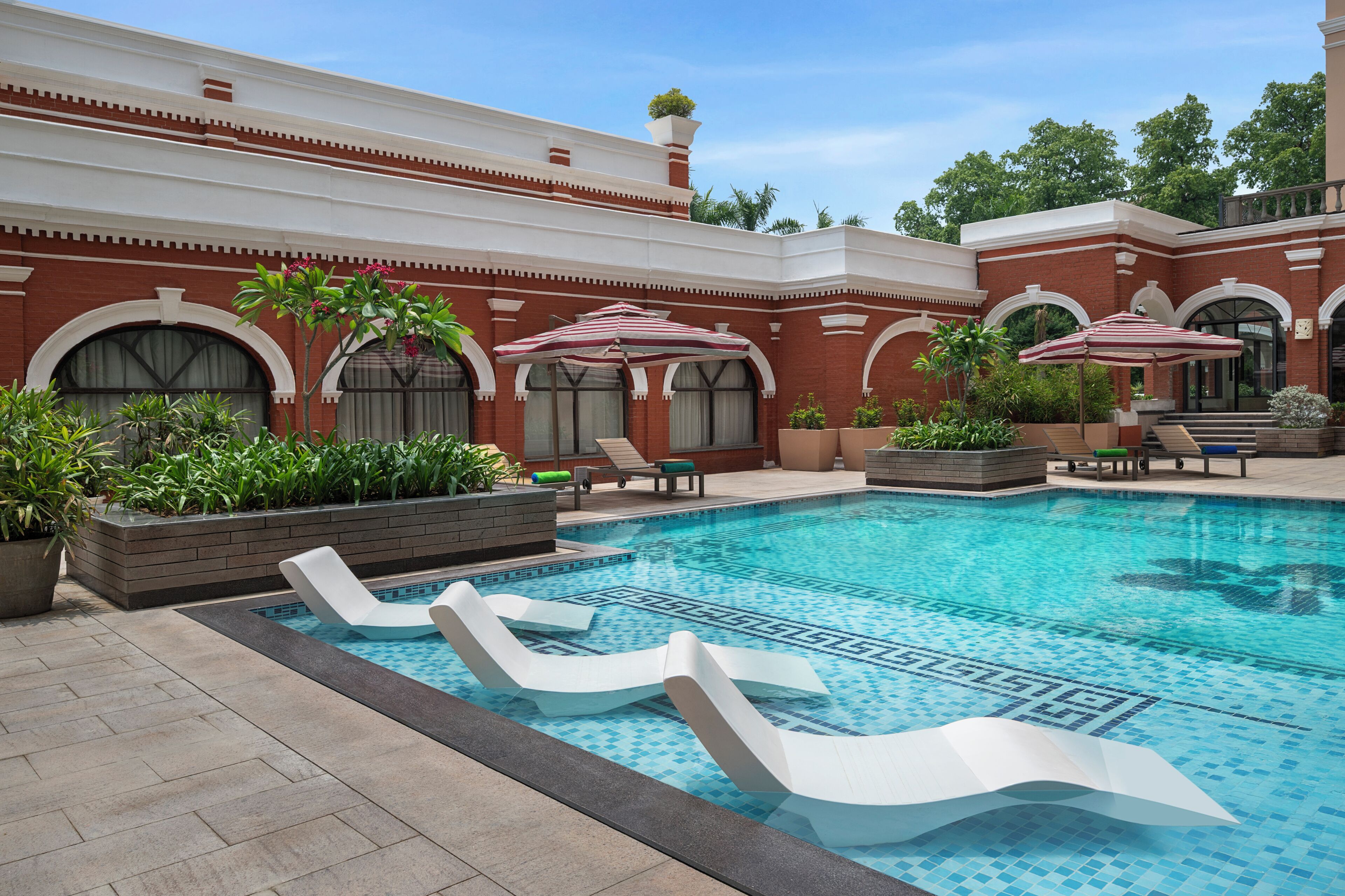 A swimming pool with lounge chairs, potted plants, and umbrellas.