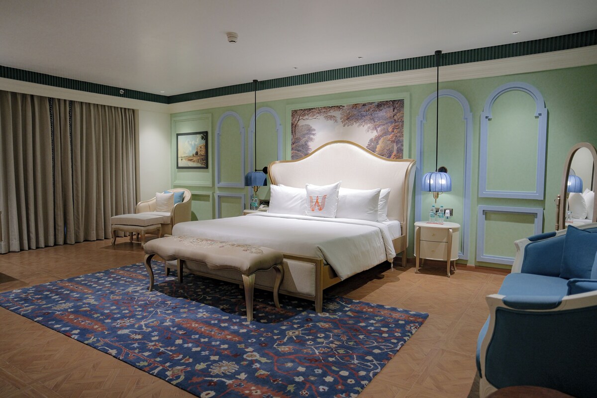 Ein Schlafzimmer mit einem großen Bett, einem Sessel, einem kleinen Tisch und einem Spiegel.