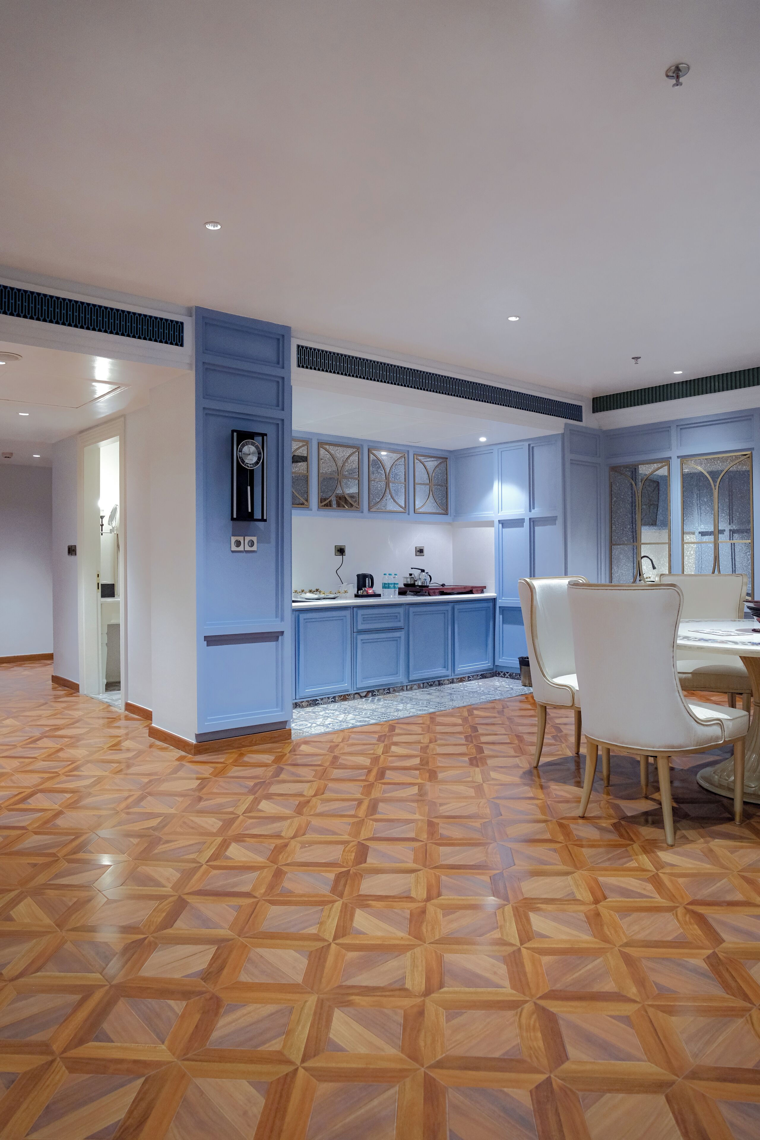 Una cocina moderna con armarios azules, un comedor con sillas blancas y un piso de madera con diseño.