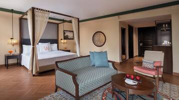 Una camera d'albergo con un letto a baldacchino, un divano, una poltrona, un tavolino con delle mele e un tappeto decorato.
