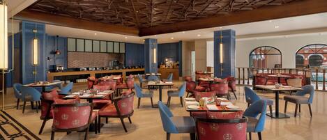 A spacious dining area with multiple tables and chairs, a bar, and a high ceiling with a geometric pattern.