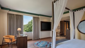 Habitación de hotel con cama, escritorio con lámpara, una silla, televisión y vistas a zonas verdes.