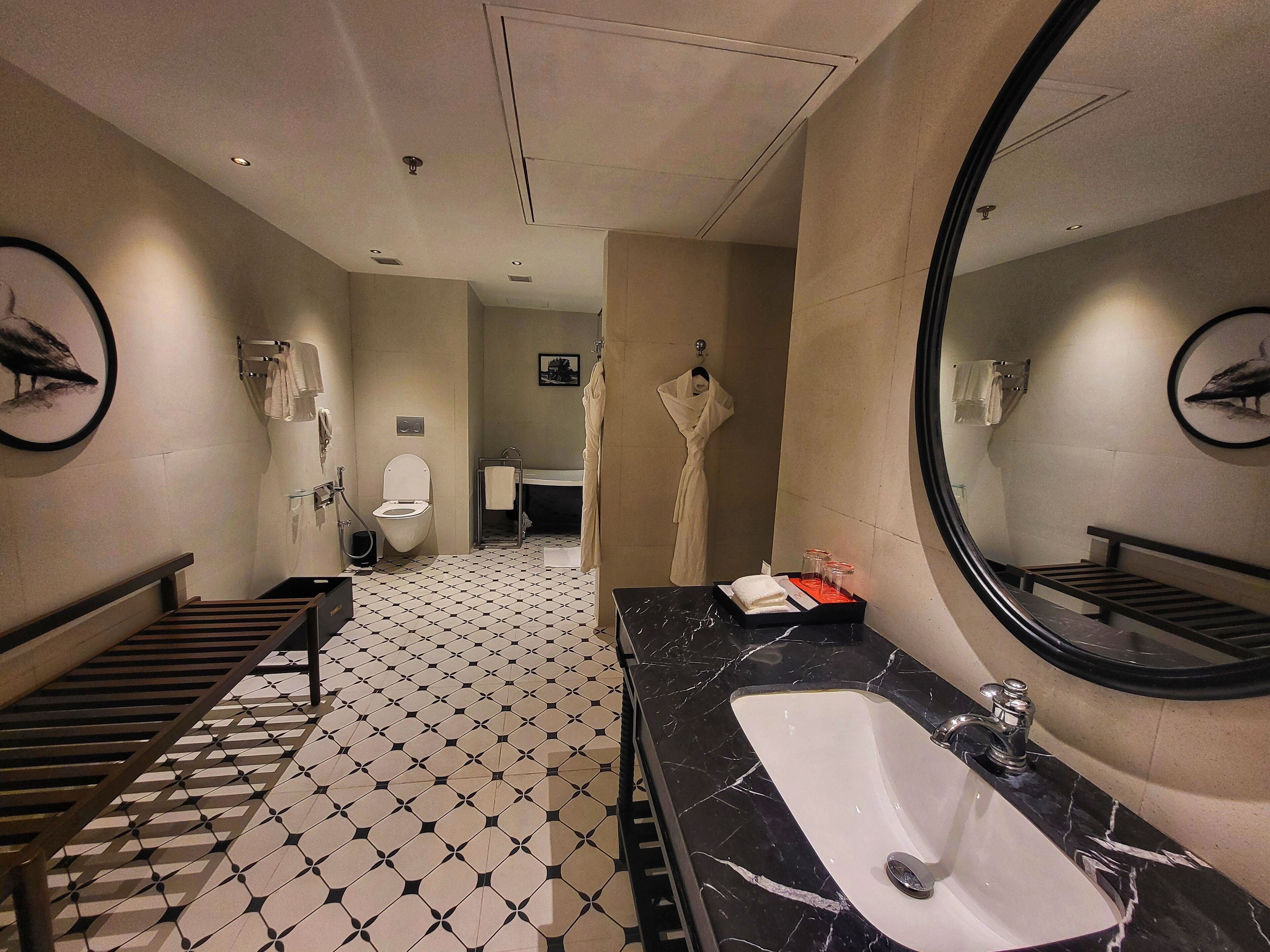 A modern bathroom with a black and white tiled floor, a large mirror, a sink, and a toilet.