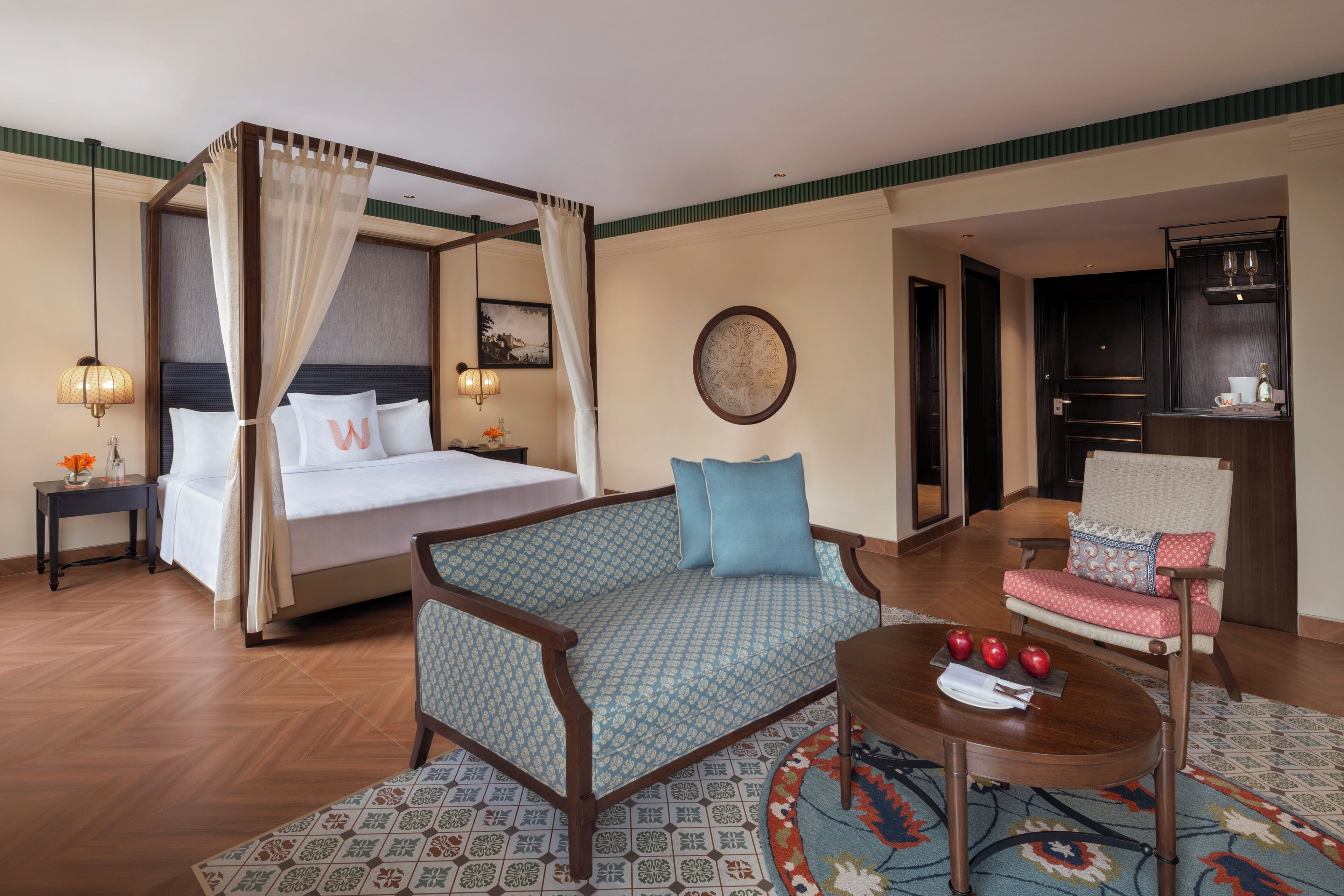 A hotel room with a four-poster bed, a sofa, a chair, a small table, and a decorative rug.