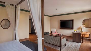 Habitación de hotel con cama, escritorio, silla, televisor y ventana con cortinas.