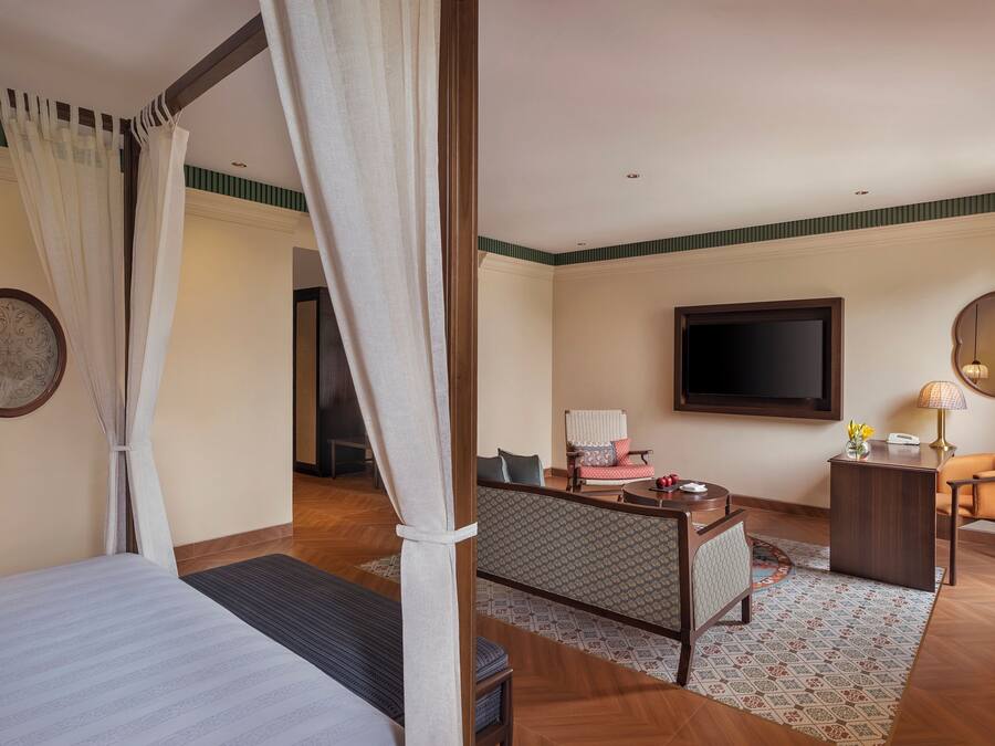 Habitación de hotel con cama, escritorio, silla, televisor y ventana con cortinas.
