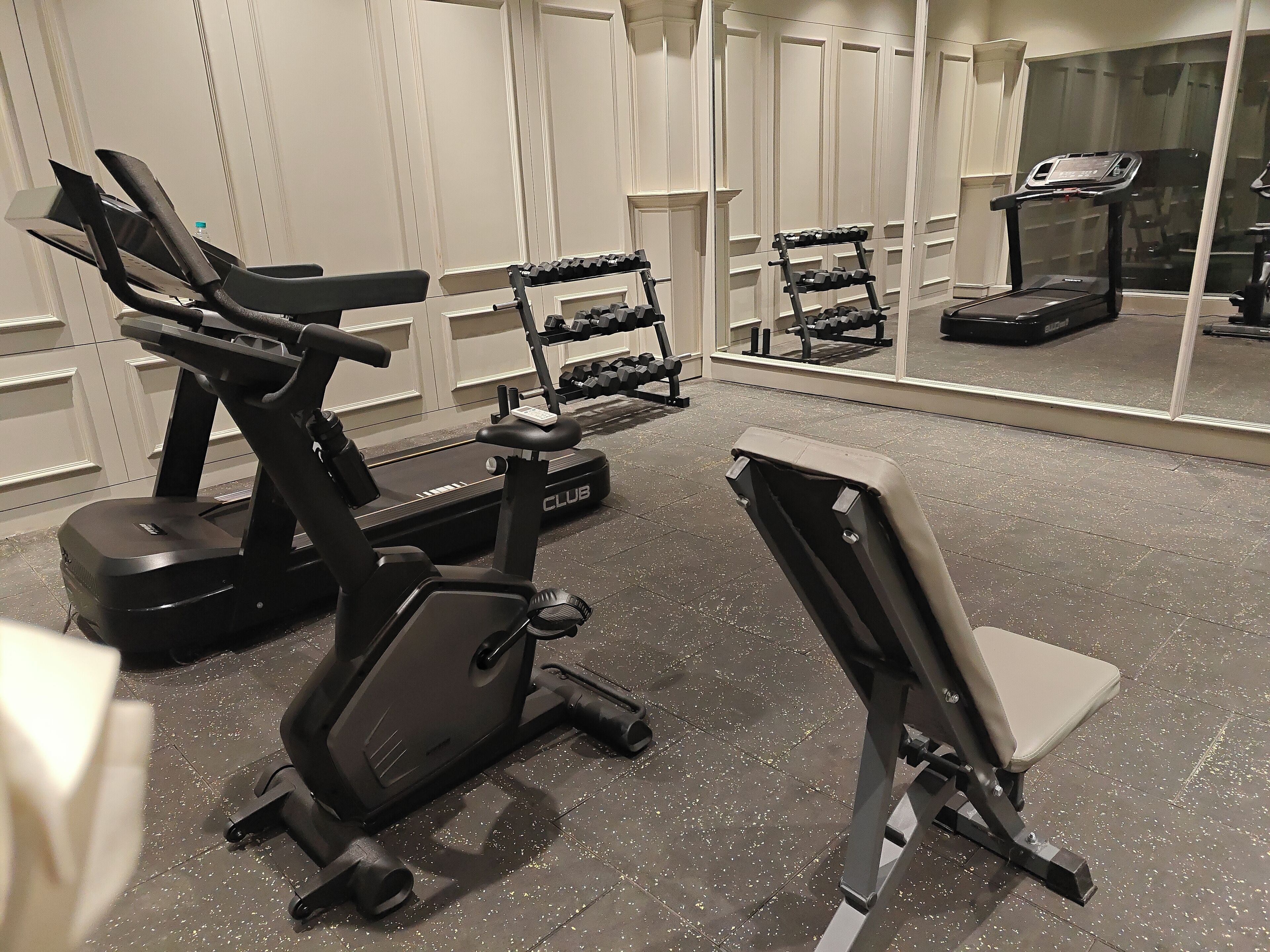 Ein Fitnessraum mit Trainingsgeräten, darunter Laufbänder, ein Crosstrainer und eine Bank.