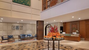 Un vestíbulo de hotel con un mostrador de recepción, un área de estar azul y una mesa decorativa con flores.