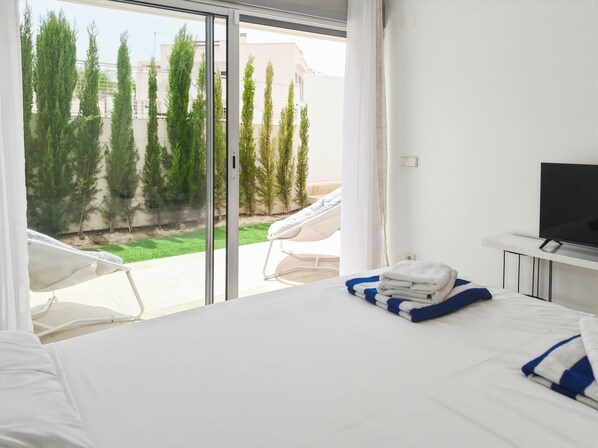 Ein Hotelzimmer mit Bett, Fernseher und Blick auf einen Garten mit Bäumen und einer Hängematte.