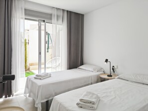 Ein Hotelzimmer mit zwei Betten, einem kleinen Tisch, einem Stuhl und einem Fenster mit Vorhängen.