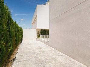 A modern building with a flat roof, a concrete pathway, and a row of evergreen trees on one side.