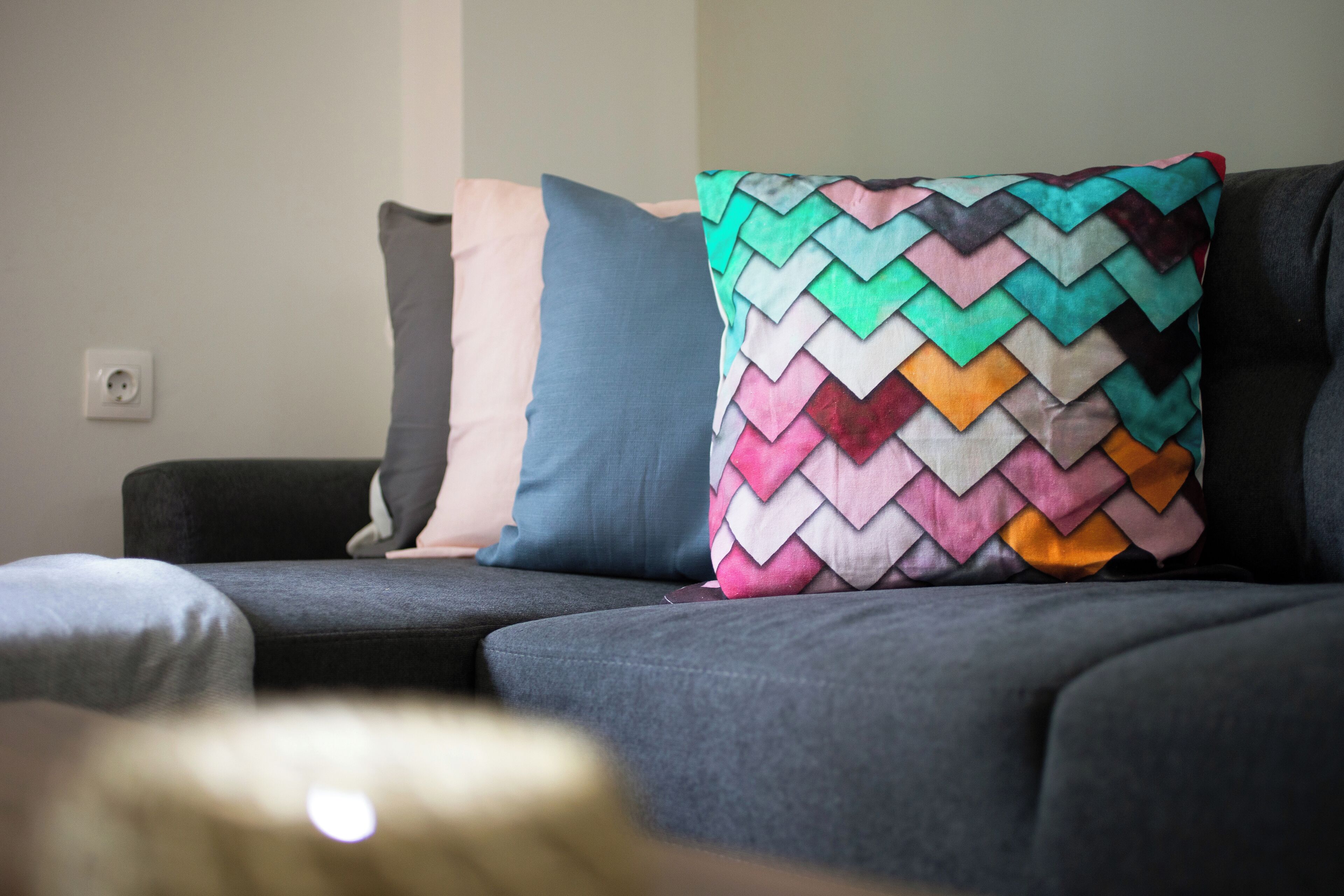 A grey sofa with three pillows in different colors and patterns.