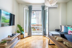 En moderne stue med trægulv, sofa, fjernsyn og et spiseområde med bord og stole.