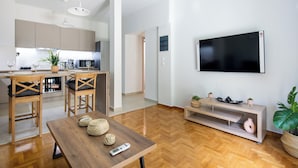 Une cuisine moderne avec des meubles en bois, un coin repas avec une table en bois et un salon avec un téléviseur et une plante.