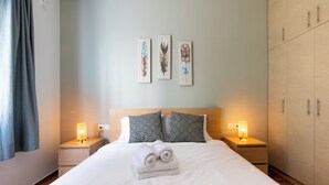 Un lit bien fait, avec des serviettes pliées, une tête de lit agrémentée de deux coussins, des lampes de chevet et trois œuvres d’art murales en plumes.