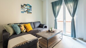 A modern living room with a grey sofa, a coffee table, and a balcony with curtains. - Theai 1-Bedroom Apartment in Athens (Athens)