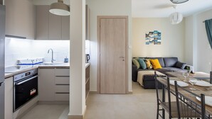 A modern kitchen with built-in appliances, a dining area with a table set for two, and a living area with a sofa and cushions. - Theai 1-Bedroom Apartment in Athens (Athens)