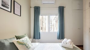 A bedroom with a bed, a window with curtains, a wall-mounted air conditioner, and a door. - Theai 1-Bedroom Apartment in Athens (Athens)