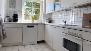 A modern kitchen with white cabinets, a Bosch dishwasher, a coffee maker, and a window with a view of trees. - Strandgut - Half of a house in the center of Zingst (Zingst)
